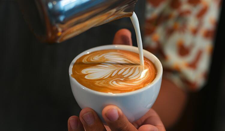 Milch wird in einen Kaffee gegossen